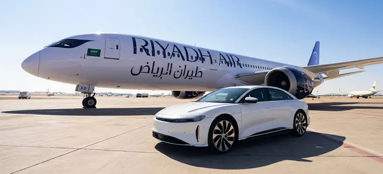 Riyadh Air aircraft parked on the tarmac at Riyadh Airport with a white luxury electric sedan in the foreground on a sunny day.