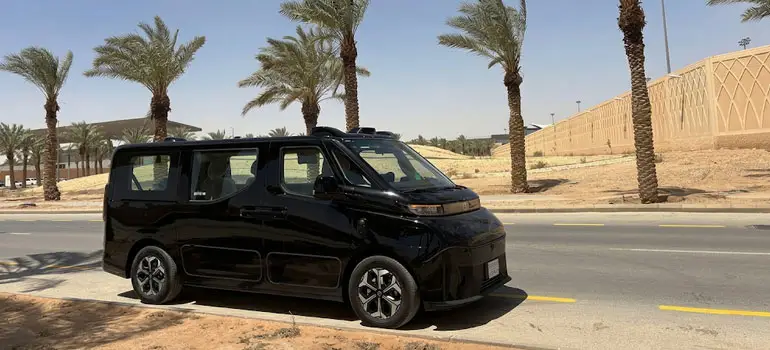 Modern black autonomous electric shuttle van parked on a palm-lined street in Al Ula.