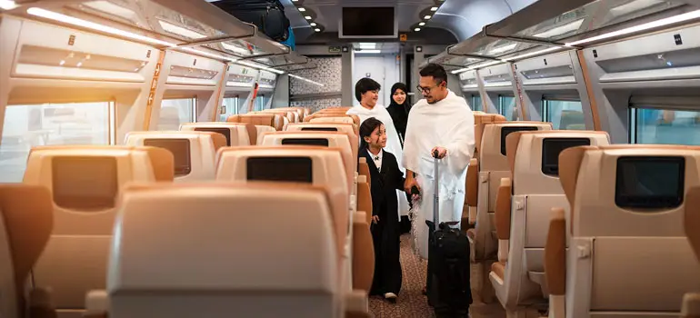 Muslim family in Ihram clothing walking down the aisle of a Haramain train carriage on their journey between Jeddah and Madinah.