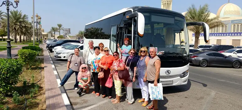 Tour group posing in front of a white coach bus near a mosque in Saudi Arabia.