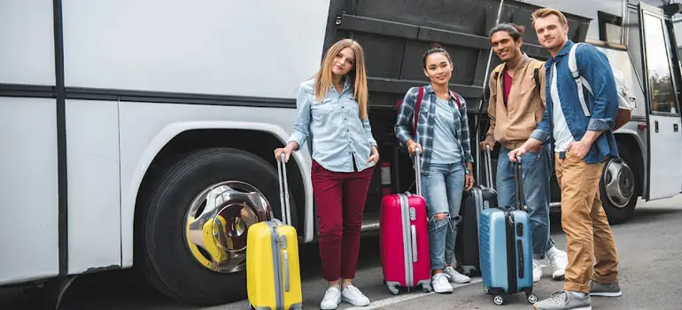 Young travelers with colorful suitcases standing beside a white tour bus in Saudi Arabia.