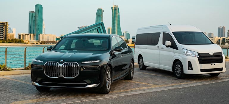 Luxury BMW sedan and white private van for transport services with Dammam city skyline in the background.
