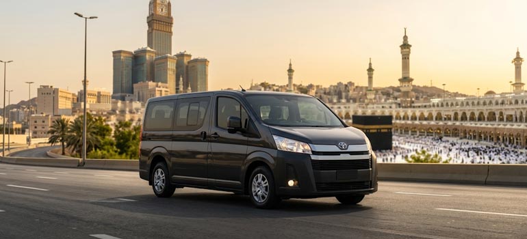 Luxury private van on the road with Makkah Clock Tower and Qahba in the background for Jeddah to Makkah transport.