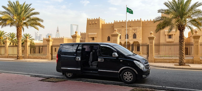 Black luxury van for private transport service parked near historic palace and Kingdom Centre skyline in Riyadh.