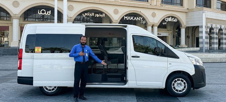 Professional chauffeur with white private van ready for group transport service in Riyadh city center.